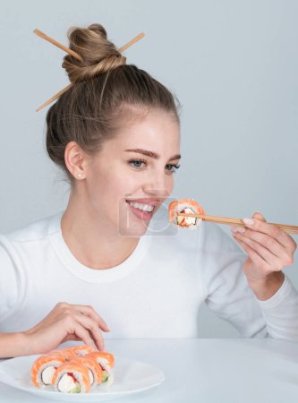 Téléchargez les photos : Fun jeune femme manger des sushis sur fond gris. Gros plan portrait de beauté femme manger sushi rouleaux - en image libre de droit