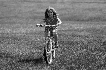 Foto de Un niño pequeño monta en bicicleta en el parque. Chico en bicicleta. Feliz niño sonriente montando una bicicleta. El chico empieza a andar en bicicleta. Deportiva bicicleta para niños montando en la hierba. Bicicleta infantil - Imagen libre de derechos