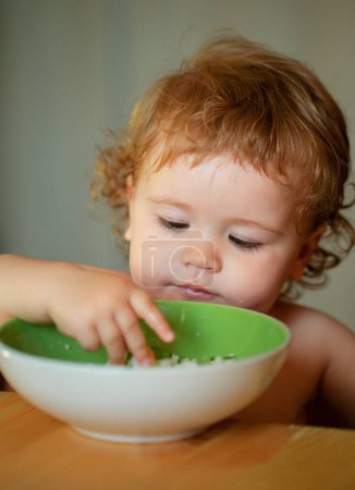 Photo for Healthy nutrition for kids. Portrait of cute Caucasian child kid with spoon. Hungry messy baby with plate after eating - Royalty Free Image
