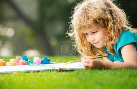 Téléchargez les photos : Enfant garçon appréciant l'art et l'artisanat dessin dans la cour arrière ou parc de printemps. Les enfants dessinent avec des crayons en plein air. passe-temps des enfants, enfance heureuse - en image libre de droit