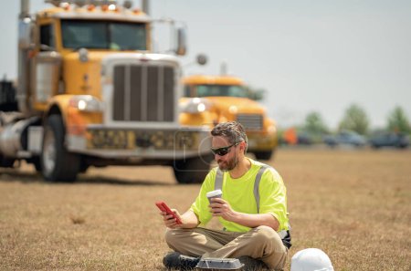 Téléchargez les photos : Travailleur prenant une pause du travail en buvant du café et se reposant sur l'herbe. Ouvrier constructeur détendu après le travail pendant la pause café. Pause ouvrière temps de détente. Travailleur en pause déjeuner. Chauffeur de camion - en image libre de droit