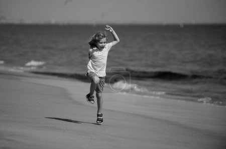 Téléchargez les photos : Petit garçon courant sur le sable près de la plage de la mer. Enfant sportif courant dans la nature. actif sain enfant garçon coureur courir en plein air - en image libre de droit