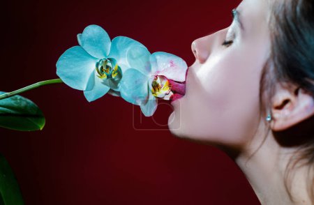 Foto de Sexy chica lamer flor de orquídea. Orquídeas lengua oral. Sensual joven mujer chupar orquídea floral. Liras rojas con lápiz labial - Imagen libre de derechos