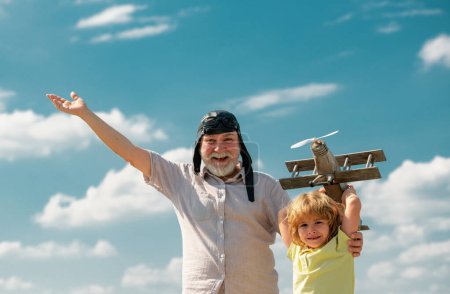 Téléchargez les photos : Vieux grand-père et jeune petit-fils enfant avec avion jouet sur fond bleu ciel et nuages. Hommes génération grand-père et petit-fils jouer à l'extérieur - en image libre de droit