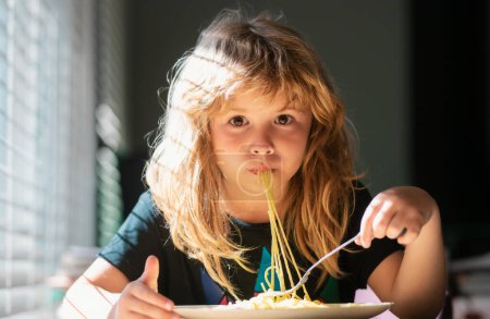 Cute little kid eating spaghetti pasta at home. Close up portrait of funny kid eating. Little boy having breakfast in the kitchen