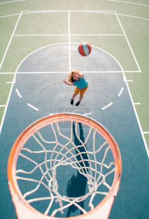 Téléchargez les photos : Enfant en uniforme de basket-ball sautant avec balle de basket pour tir sur le terrain de basket - en image libre de droit