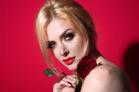 Téléchargez les photos : Femme séduisante tenant rose rouge. Beau modèle avec fleur de rose rouge, isolé sur fond de studio rouge. Charmante jeune fille avec un maquillage parfait - en image libre de droit