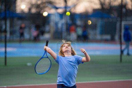 Téléchargez les photos : Enfant jouant au tennis sur le terrain. Blond petit garçon frappé balle de tennis avec raquette de tennis. Exercice actif pour les enfants. Activités estivales pour les enfants. Enfant apprenant à jouer au tennis. Sport Kid frapper balle - en image libre de droit