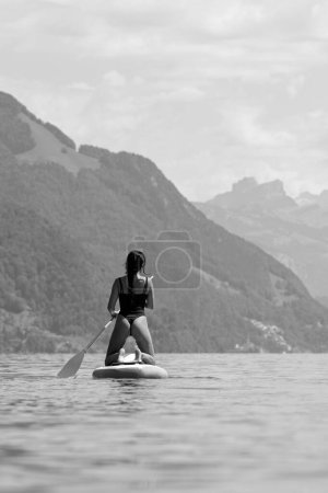 Photo for Sexy back of fit woman with paddle board. Black and white. Woman paddling on paddleboard. SUP surfing in summer vacation in Alps lake in Swiss. Sexy summer - Royalty Free Image