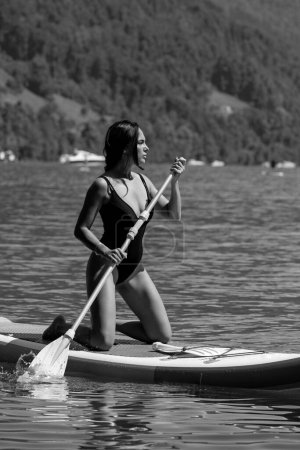 Vacaciones de verano. Mujer sexy remando en el tablero de paddle o cenar en el lago. Estilo de vida. Modelo de punto de ajuste femenino nadando con tabla de paddle