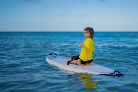 Kind schwimmt auf Paddelbrett. Wassersport, aktiver Lebensstil. Kind paddelt auf einem Paddelbrett im Ozean. Kinderpaddel-Grenze. Sommer-Wassersport, SUP-Surfen. Sommerurlaub am Strand