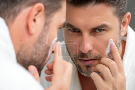 Man applying face cream. Beauty routine. Man with perfect skin. Anti-aging and wrinkle cream. Concept of male beauty. Close up face of man applying cream to skin. Skincare and cosmetics concept