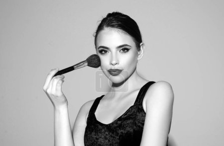 Photo for Beautiful young woman with clean fresh skin. Beautiful brunette young woman applying powder on her cheeks with a cosmetic brush - Royalty Free Image