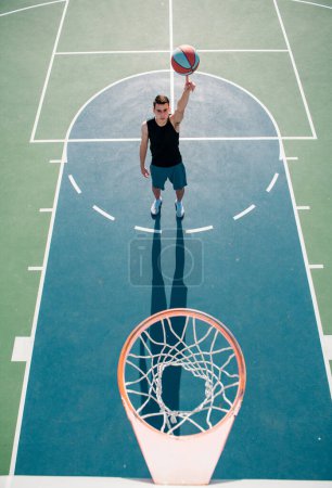 Winkelaufnahme des Mannes beim Basketballspielen, über dem Korb des Mannes beim Basketballschießen. Handspinnender Korbball. Basketball auf dem Finger balancieren