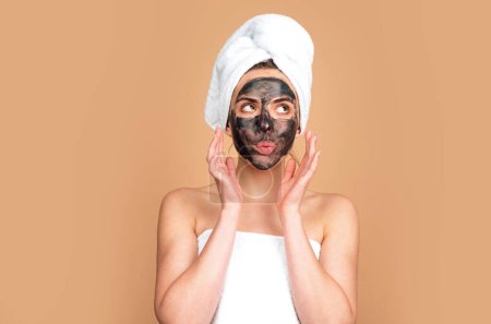 Photo for Woman apply charcoal facial mask mask isolated over beige studio background. Spa, cosmetic mask. Beautiful woman with black clay facial mask. Skin care, peeling, moisturising and beauty treatment - Royalty Free Image