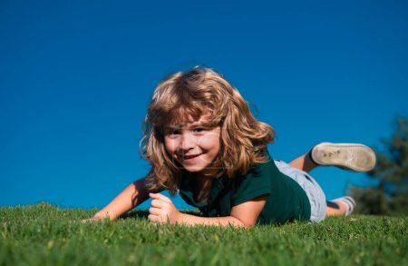 Foto de Retrato de un niño feliz tirado en el césped del parque. Retrato al aire libre de un niño bonito sobre hierba verde fresca. Diversión de verano, infancia feliz - Imagen libre de derechos