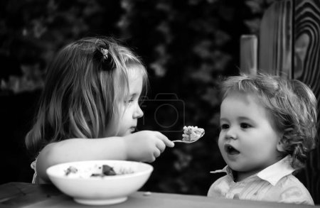 Foto de Hermana alimentando hermano. La chica alimenta al niño con una cuchara. Comida para niños. - Imagen libre de derechos