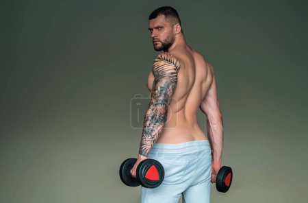 Photo for Muscular man pumps his muscles and lifts dumbbells in gym. Strong fit man exercising with dumbbells. Muscular young handsome man lifting weights. Weightlifting and training with dumbbells - Royalty Free Image