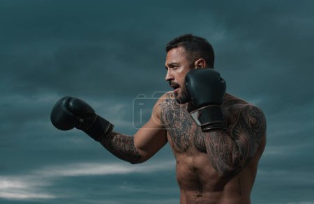 Téléchargez les photos : Entraînement de boxeur en plein air. boxeur sportif muay thai combat dans des gants. Homme sportif pendant les exercices de boxe. Force, concept d'attaque et de mouvement. Entraînement de boxe dehors. Corps de l'homme musculaire - en image libre de droit