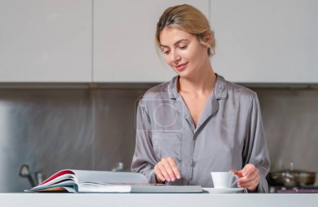 Photo for Sexy woman drink coffee and reading book or magazine at home in morning. Beautiful sensual female housewife have breakfast in sexy pajama at kitchen - Royalty Free Image