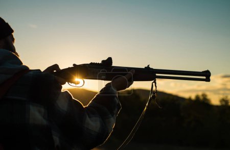 Un cañón de un arma. Rifle Hunter Silhouetted en Beautiful Sunset. Cazador con Fusil Poderoso con Alcance Spotting Animals. Copiar espacio para texto
