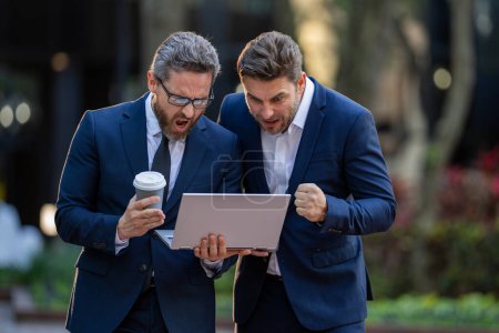 Business men were dedicated to their teams success. Project planning. Surprized business men team using laptop outdoor. Businessmen looking laptop with their business success in city