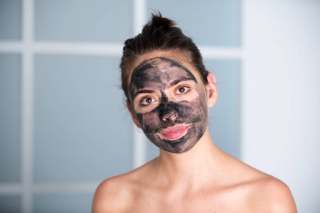 Téléchargez les photos : Woman with charcoal facial mask. Beautiful young woman with facial black mud clay mask. Skin care and treatment, spa, natural beauty and cosmetology concept - en image libre de droit