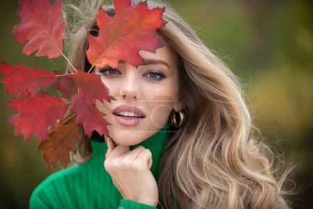 Foto de Mujer feliz sosteniendo hojas de otoño en la cara en la naturaleza otoño. Retrato de mujer joven con hojas de arce de otoño al aire libre. Chica bonita jugar con la hoja de otoño caminando en el parque. Otoño cálido. Otoño temporada moda - Imagen libre de derechos
