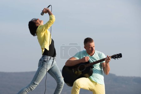 Photo for Excited sexy couple enjoy music with microphones and guitar. Sexy couple dancing and singing outdoor. Carefree couple sing hold mic and guitar. Couple in love singing and playing guitar outdoors - Royalty Free Image