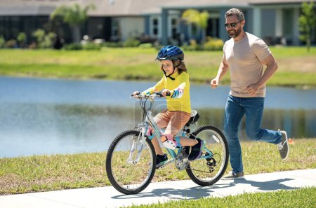 Père et fils en casque de vélo pour apprendre à faire du vélo au parc. Père aidant son fils à faire du vélo. Père et fils sur le vélo le jour de l'été. Petit fils essayant de faire du vélo avec son père. Fête des pères