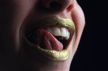 Téléchargez les photos : La langue sexy lèche les lèvres. Sensuelle femme souriante heureuse bouche. Fille sexy lèvres dorées, bouche dorée. Peau dorée éclatante et lèvres dorées. Brillance métallique brillant à lèvres doré - en image libre de droit