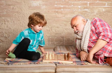 Téléchargez les photos : Petit garçon jouant aux échecs avec son grand-père. Pièce d'échecs. Senior homme penser à son prochain mouvement dans un jeu d'échecs - en image libre de droit