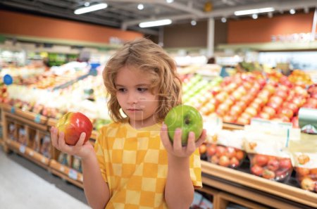 Foto de Los niños tienen frutas de manzana en la tienda de comestibles. Pequeño niño eligiendo comida en la tienda de comestibles o en un supermercado - Imagen libre de derechos