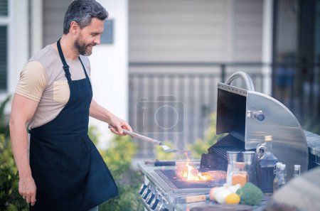 Photo for Barbecue concept. Middle aged hispanic man in apron for barbecue. Roasting and grilling food. Roasting meat outdoors. Barbecue and grill. Cooking meat in backyard - Royalty Free Image