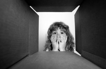 Foto de Divertido niño emocionado está abriendo regalo y mirando dentro de la caja de cartón. Parcelas y entrega - Imagen libre de derechos
