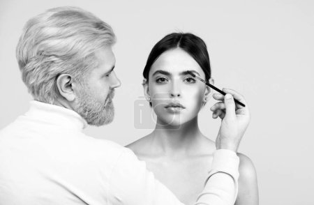 Foto de Hombre profesional visagiste maquillaje artista peinado cejas. Peina las cejas con un cepillo en un salón de belleza. Mujer con pestañas largas y cejas gruesas - Imagen libre de derechos