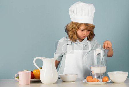 Photo for Child chef isolated on blue. Funny little kid chef cook wearing uniform cook cap and apron cooked food with flour in the kitchen - Royalty Free Image
