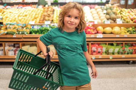 Téléchargez les photos : Enfants avec panier. Le gamin choisit des légumes et des fruits frais dans le magasin. Enfant achetant de la nourriture dans un supermarché - en image libre de droit
