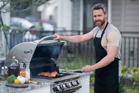 Cropped image of handsome man is making grill barbecue outdoors on the backyard. Bbq party. Bbq meat, grill for picnic. Roasted on barbecue. Man preparing barbeque in the house yard