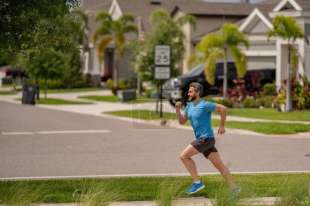 Foto de Un apuesto hombre de mediana edad corriendo por el vecindario americano. Hombre atlético corriendo al aire libre. Estilo de vida saludable. Corredor sano activo trotando al aire libre - Imagen libre de derechos