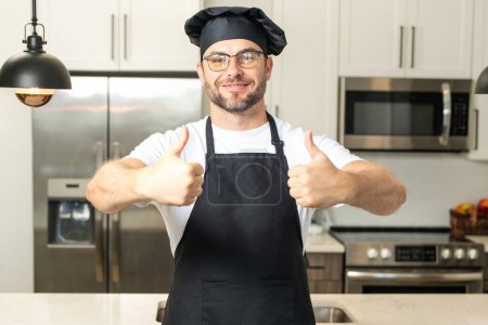 Foto de Cocinero feliz con el pulgar hacia arriba. Hombre en sombrero de chef cocina en la cocina - Imagen libre de derechos