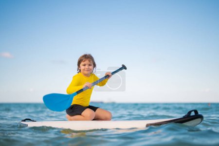 Téléchargez les photos : Enfant heureux jouant dans la mer d'été. Enfant profitant d'un stand up paddle board dans un magnifique lagon turquoise dans la mer des Caraïbes, une activité de vacances d'été saine. L'enfant monte SUP. Enfants d'été sur le conseil SUP - en image libre de droit