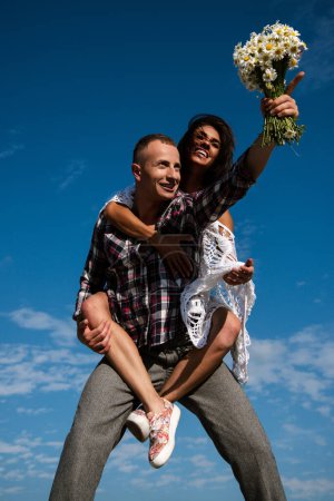 Crazy couple having fun outdoor. Young fun excited couple piggyback ride in summer day. Happy young couple having fun on summer sunny day near sky background