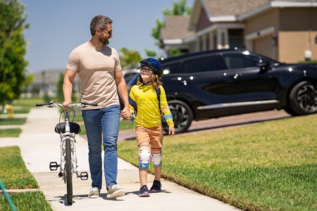 Father teaching son riding bike. Father helping excited son to ride a bicycle in american neighborhood. Child in bike helmet learning to ride cycle with his dad. Fathers day