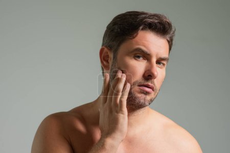 Männerpflege. Attraktiver Mann mit perfekter Haut berühren Gesicht nach der Rasur. Kosmetische Verfahren zur Hautpflege im Gesundheitswesen. Mann aus nächster Nähe mit empfindlicher Haut, männliche Kosmetologie-Behandlung. Hautpflege