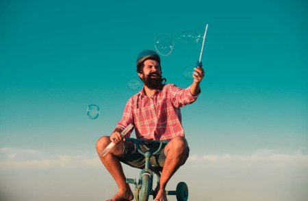 Photo for Funny man on a bicycle. Emotional crazy guy on a childrens bike. Funny young man with motorbike helmet, poses on bike, wears shirt. People, transportation and riding concept - Royalty Free Image