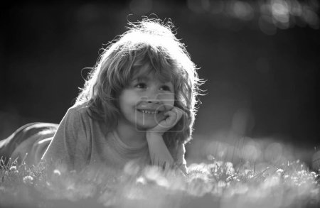 Téléchargez les photos : Portrait de petit garçon étendu sur l'herbe dans le parc naturel d'été - en image libre de droit