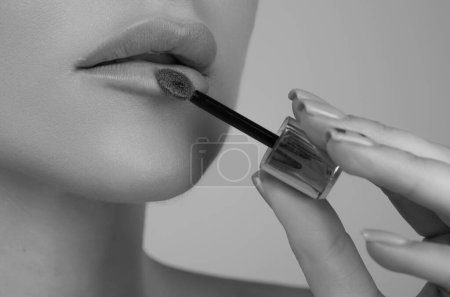 Woman puts lipstick on lips with brush. Close-up of womens hand with lipstick. Applying lipstick on lip. Professional lipstick. plumping lips. Cropped close up photo of girl apply her pomade lip stick