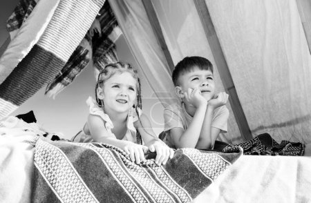 Foto de Relaciones entre hermanos. Campamento de verano. Niños en tienda casera. Lindos niños acampando. Divertirse al aire libre - Imagen libre de derechos