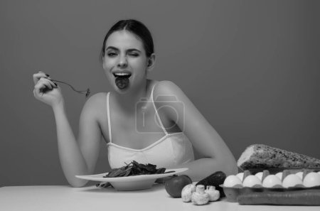Téléchargez les photos : Légumes diète. Heureuse femme souriante manger des aliments sains, suivre un régime. Fille manger de la salade de légumes régime en studio. Salade végétalienne. Femme au régime. Concept de régime. Mode de vie sain. Régime alimentaire pour perdre du poids - en image libre de droit